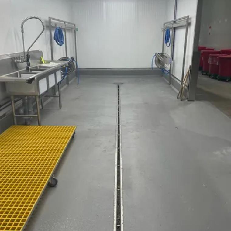 Completed stainless slot drain run in a finished food processing room with FRP grating