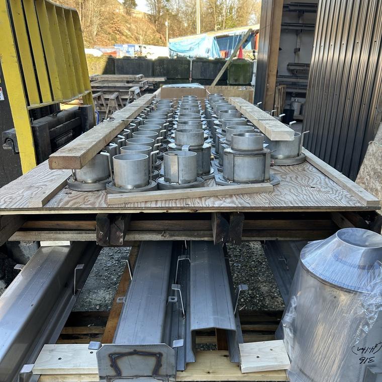 Stainless steel drain bodies and hoppers racked in the DELC shop