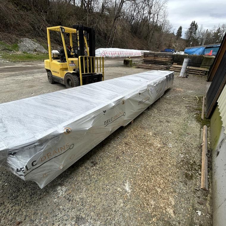 Forklift carrying a full-length wrapped stainless drain run out of the DELC shop