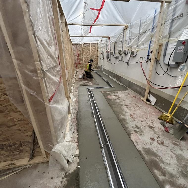 Stainless slot drain run following the wall line in a room under construction